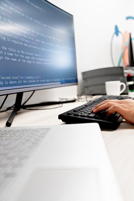 A close-up view of a person’s right hand resting on a laptop keyboard, with the thumb and fingers poised over the keys. The individual is wearing a silver wristwatch with a dark strap on their wrist